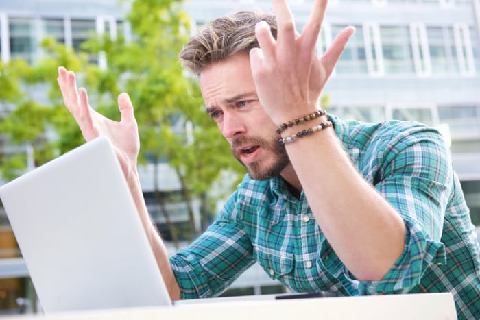 Portrait of a stressed man looking at laptop with hands raised