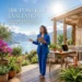 The actual hero image is of a woman standing in a blue suit holding an ipad with a sun symbol on it with a view of a lake and mountains behind her surrounded by plants and a table behind her.