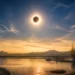 total solar eclipse above mountains, lake in middle of day
